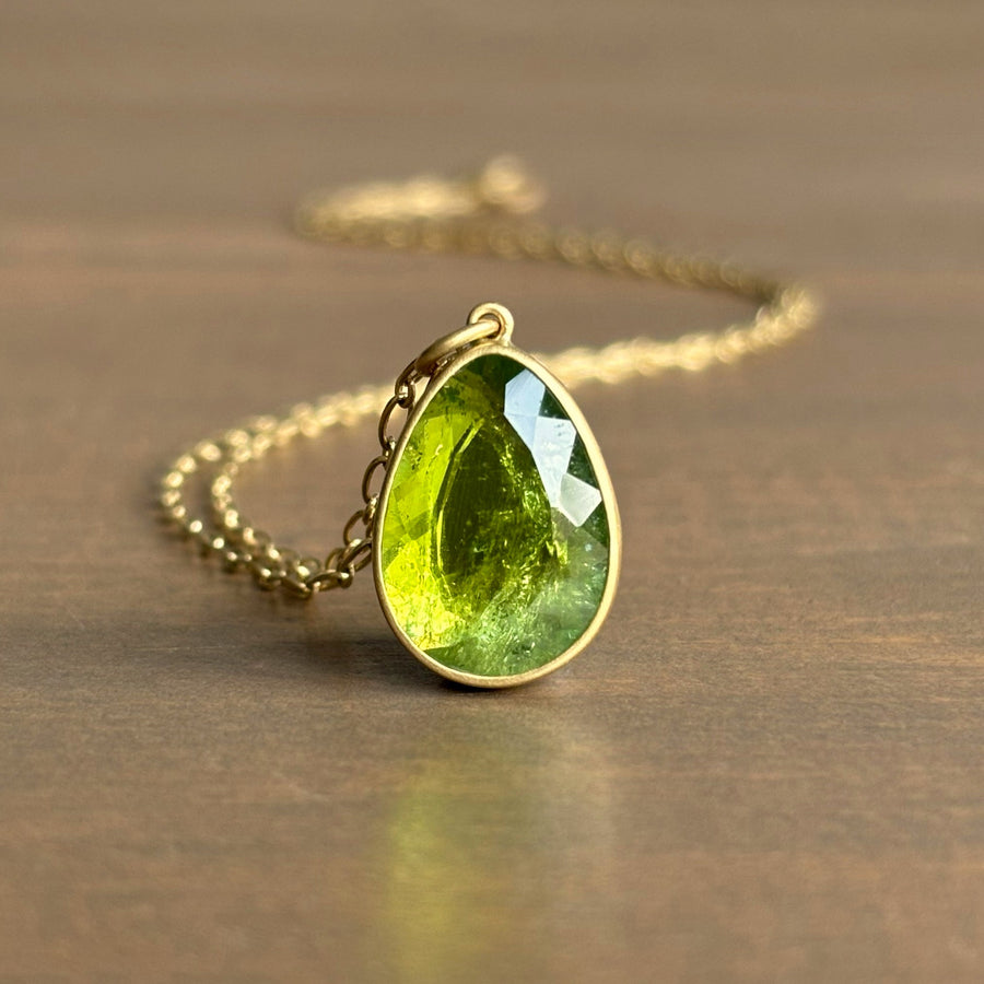 Green teardrop pendant on a gold chain against a wooden background