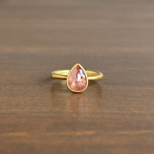 Gold ring with a teardrop-shaped pink gemstone on a wooden surface