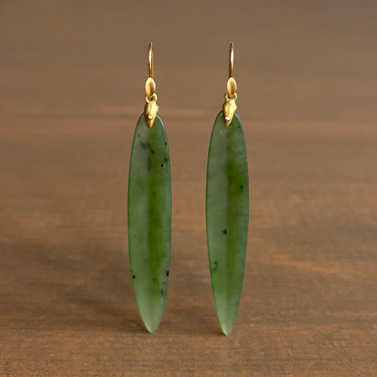 Green jade earrings with gold hooks on a brown background