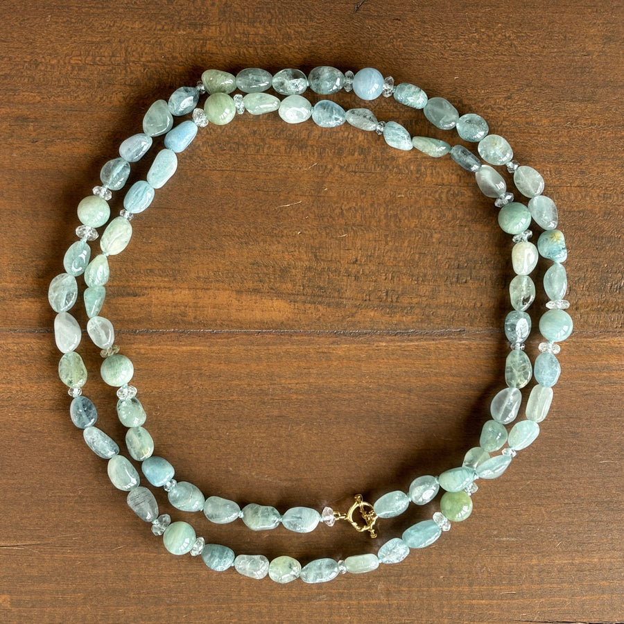 A double-strand beaded necklace made of light blue-green marbled beads with small silver spacer beads and a gold clasp, displayed on a dark brown wooden surface.
