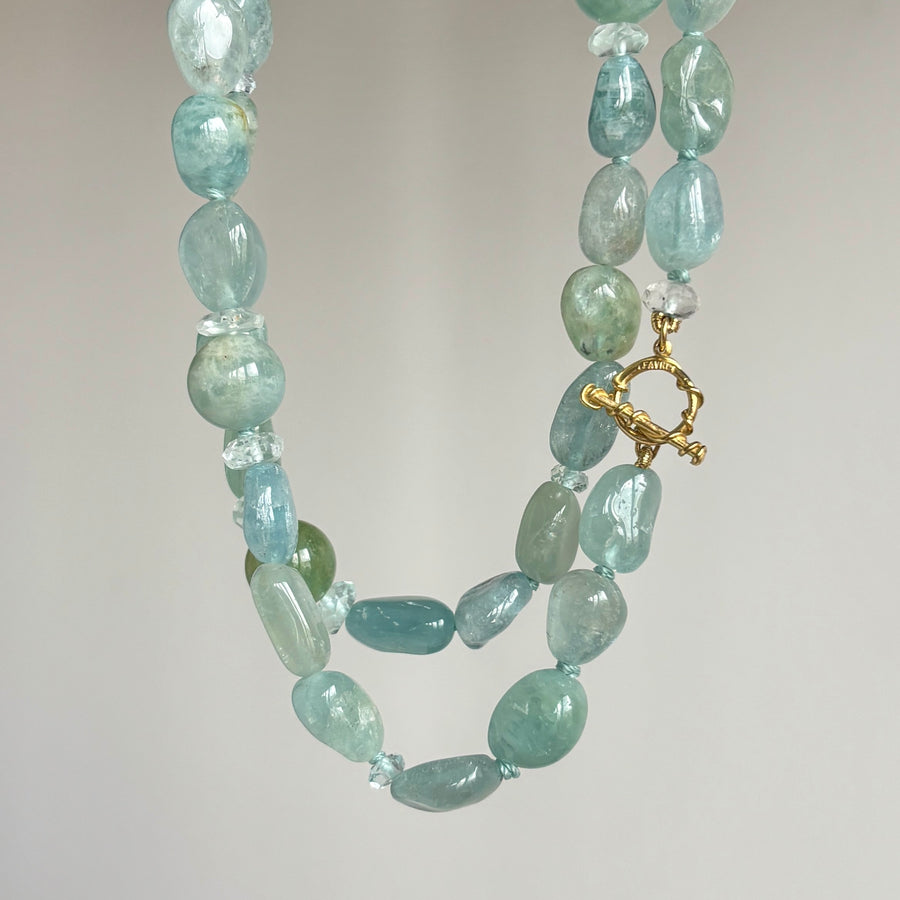 A double-strand beaded necklace made of light blue-green polished stones with a small gold toggle clasp, photographed against a plain light gray background.