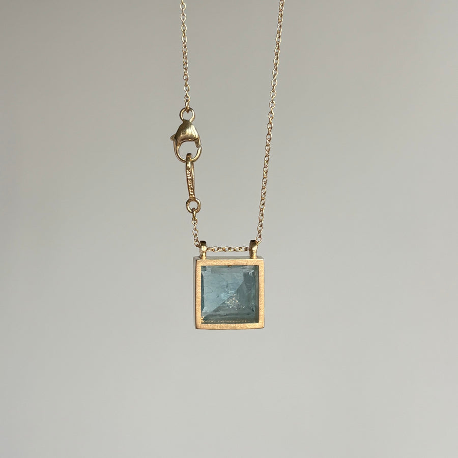 Gold necklace with a square pendant on a gray background