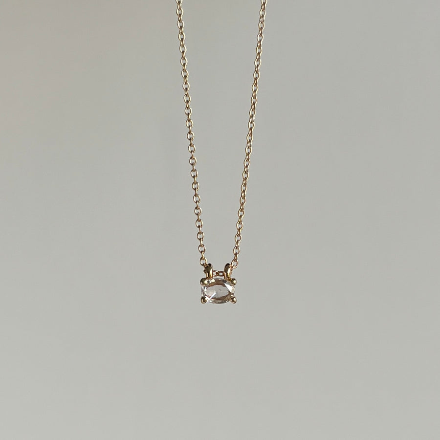 Gold necklace with a small diamond pendant on a gray background hanging