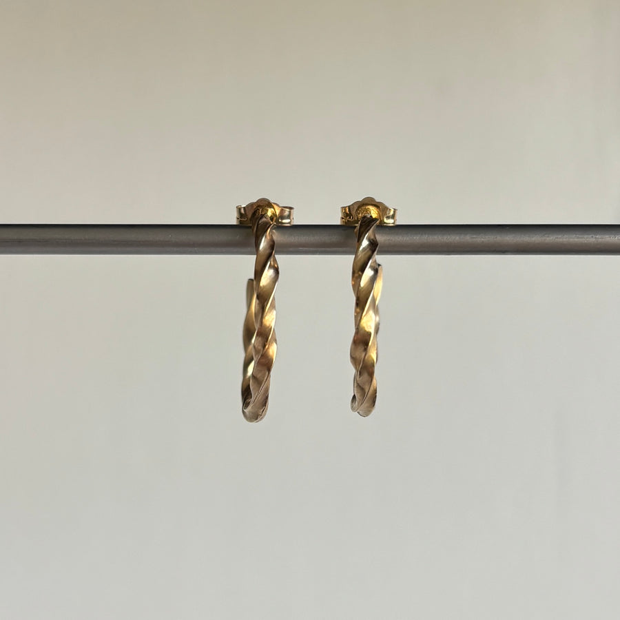 Gold hoop earrings on a thin rod against a neutral background