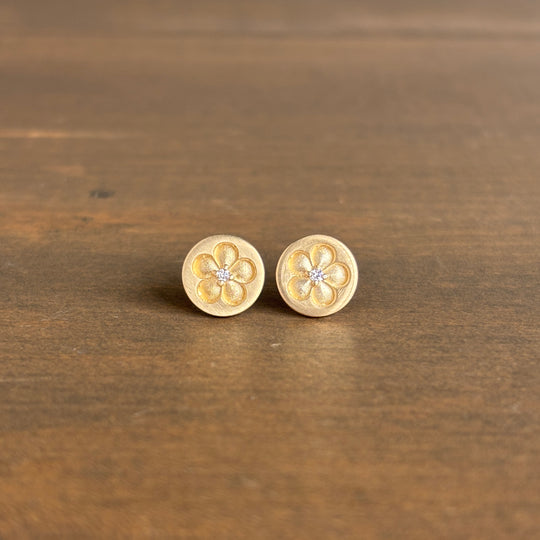 Pair of gold flower-shaped earrings on a wooden surface