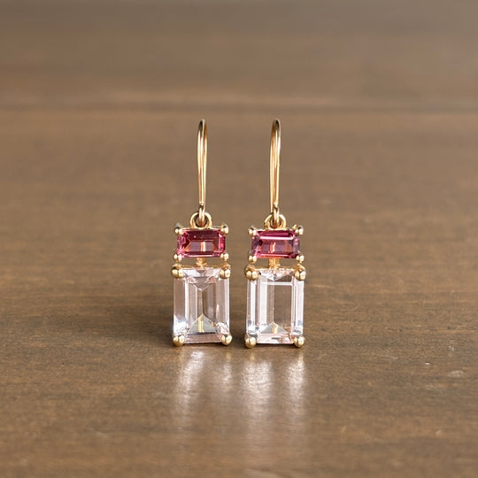 Pair of gold earrings with pink and clear gemstones on a brown surface