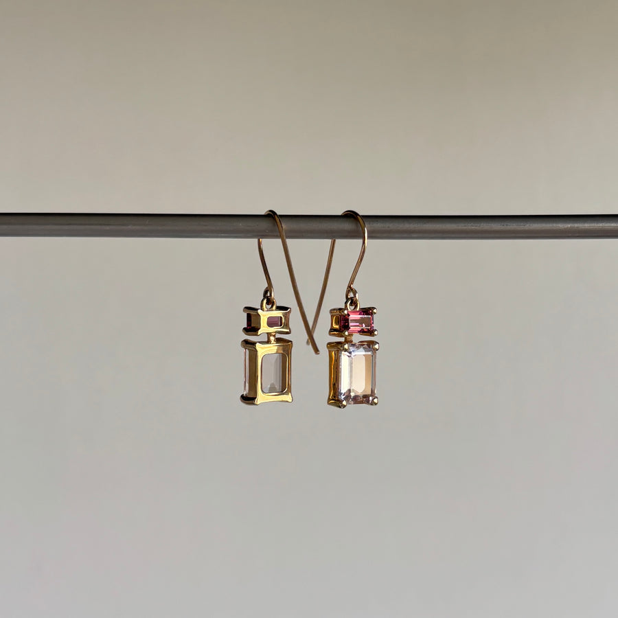 Gold and pink earrings hanging on a rod against a neutral background