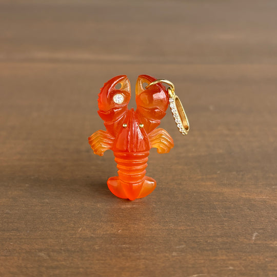 Sophie_Gardner_18k_gold_carnelian Carved orange stone lobster with gold accents on a wooden surface