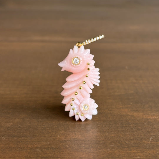Sophie_Gardner_18k_gold Pink seahorse-shaped pendant with gold accents and diamonds on a wooden surface