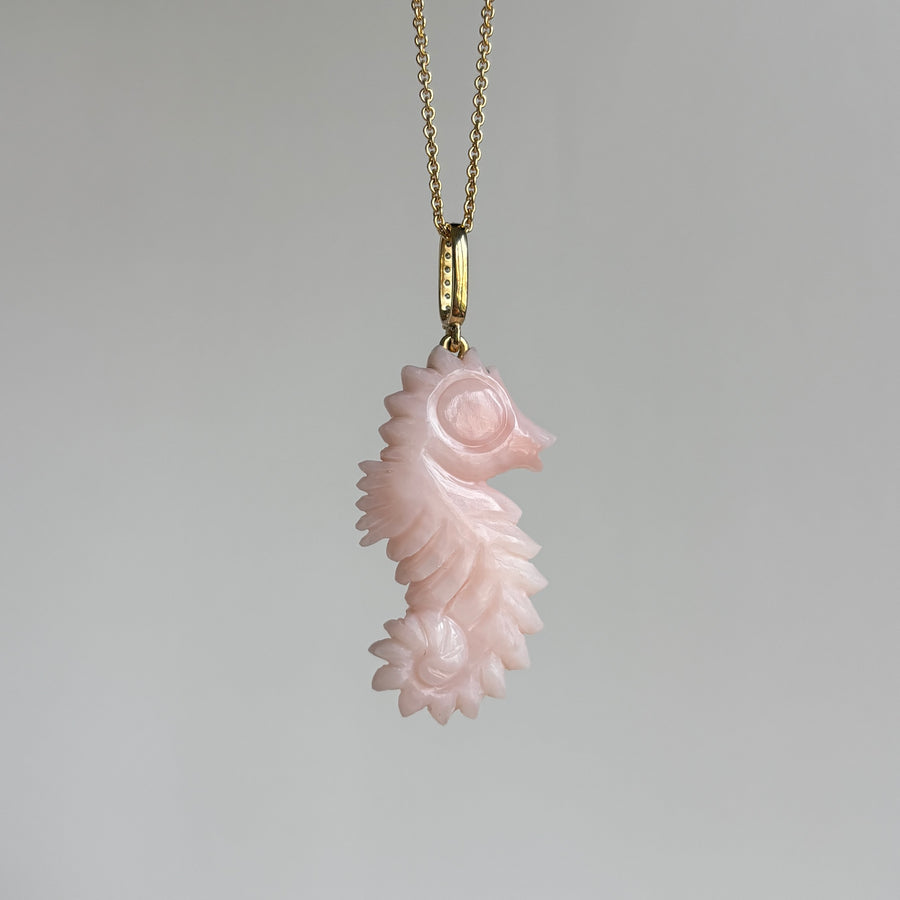 Pink seahorse pendant on a gold chain against a gray background