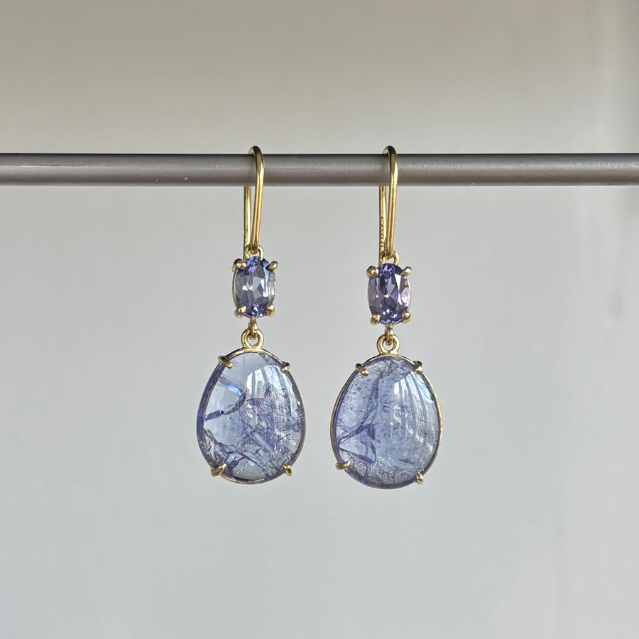 Pair of gold earrings with blue gemstones on a gray background