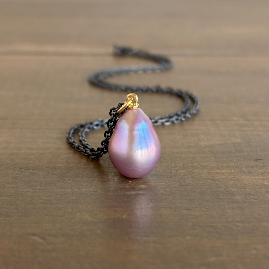 Mimi Favre Pink pearl pendant on a black chain against a wooden background