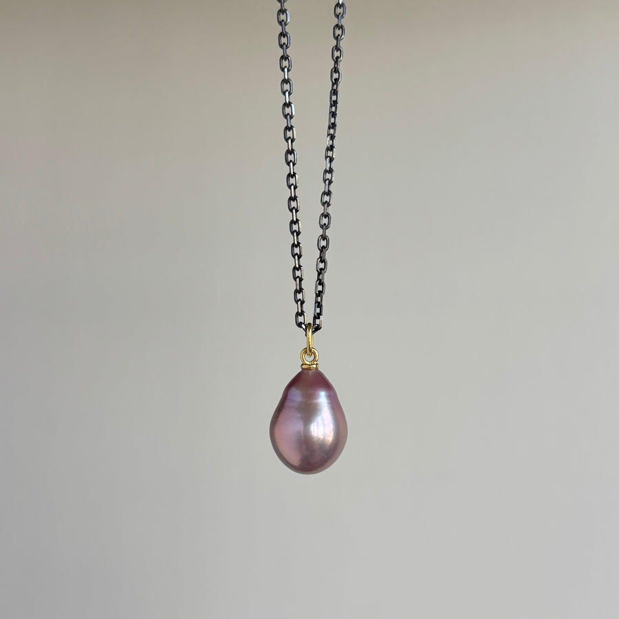 Necklace with a pink purple teardrop pendant on a chain hanging against a plain background