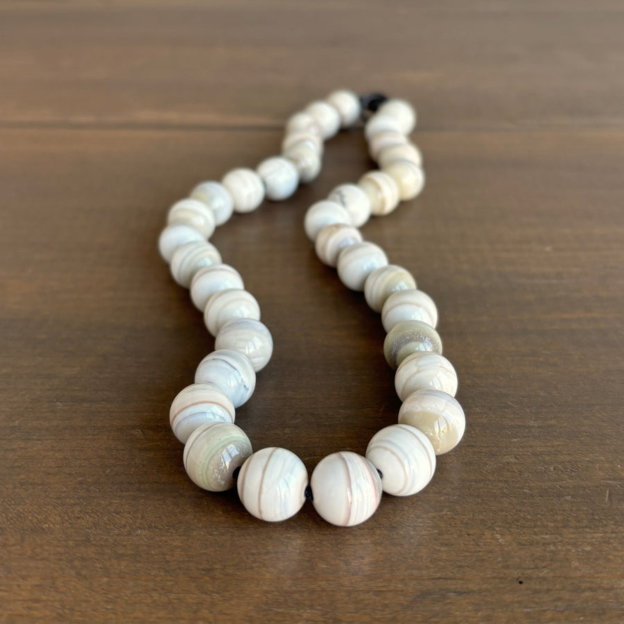 Mimi Favre Necklace with white and beige beaded pattern on a wooden surface