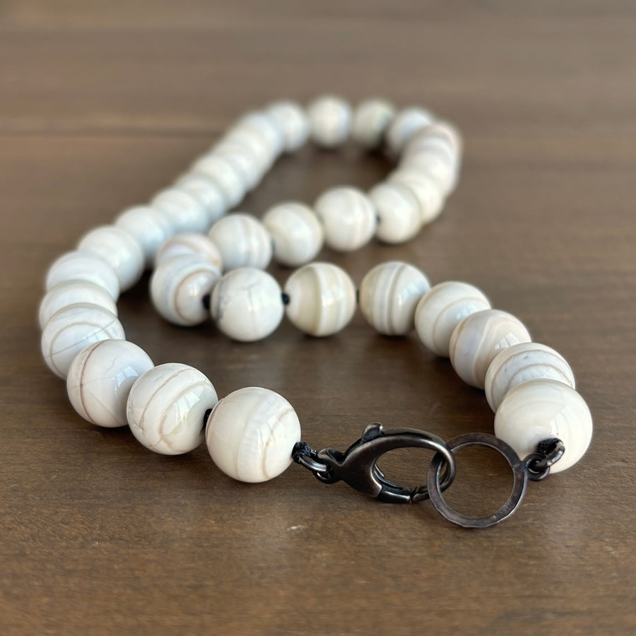 Mimi Favre Necklace with white marbled beads and a black clasp on a wooden surface