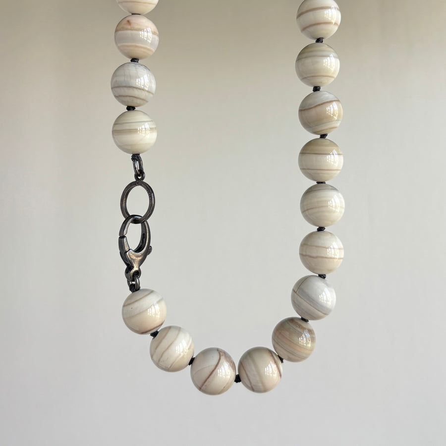 Necklace with white marbled beads on a plain background hanging