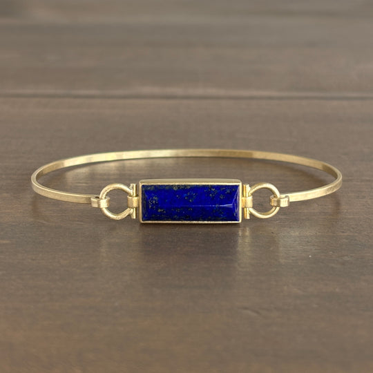 Gold bracelet with a blue stone on a dark wooden surface