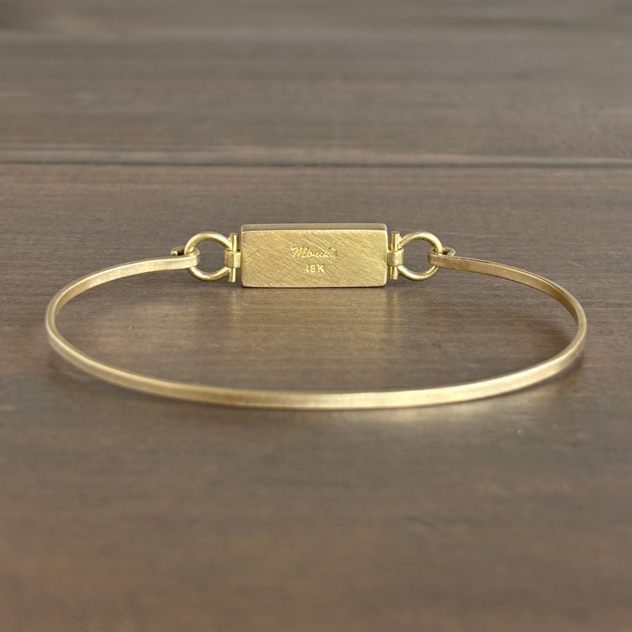 Gold bracelet with a rectangular clasp on a wooden surface