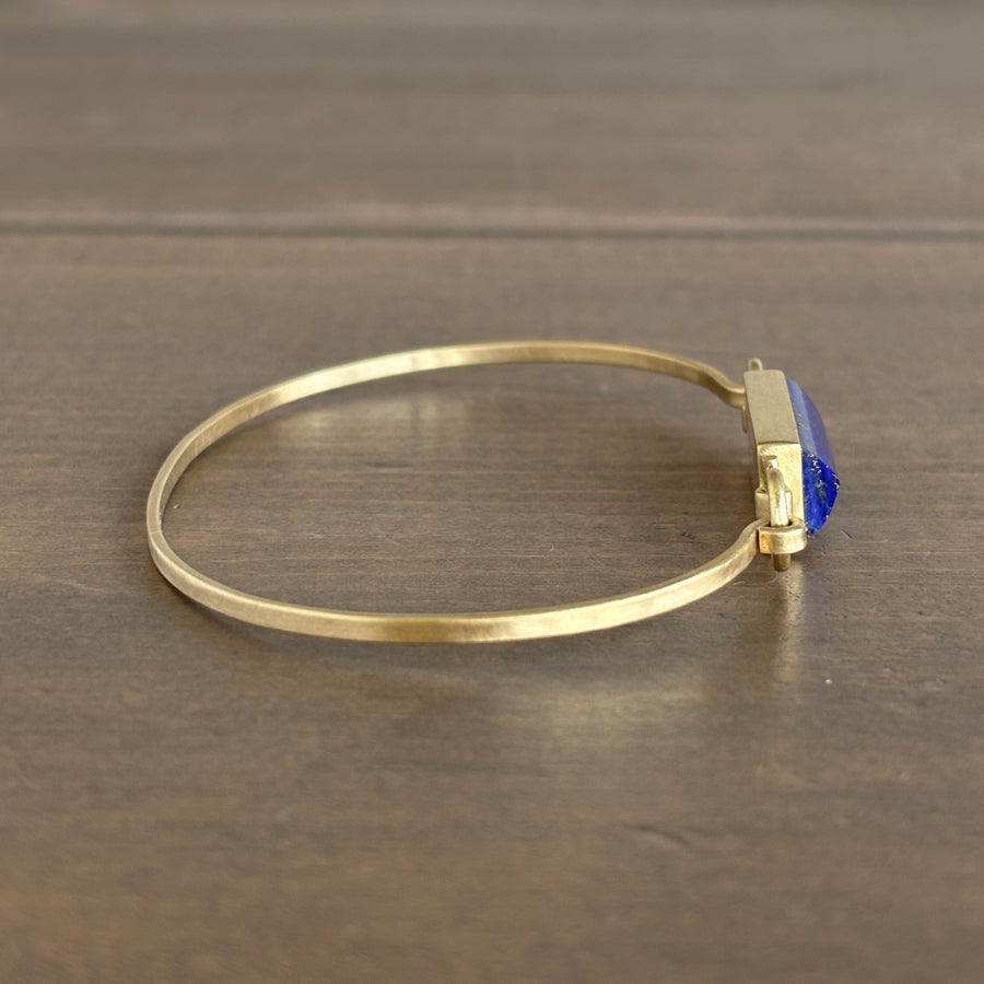 Gold bracelet with a blue gemstone on a wooden surface