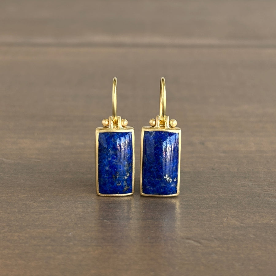 Pair of gold earrings with blue stones on a brown background