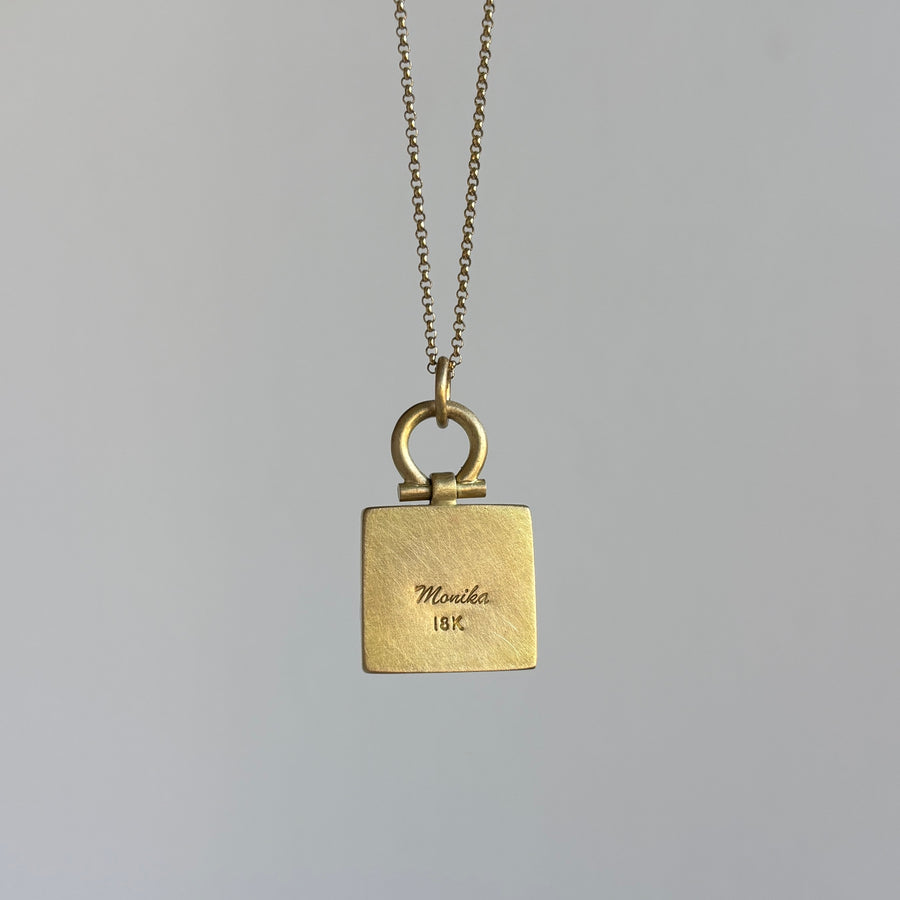Gold necklace with a square pendant on a gray background