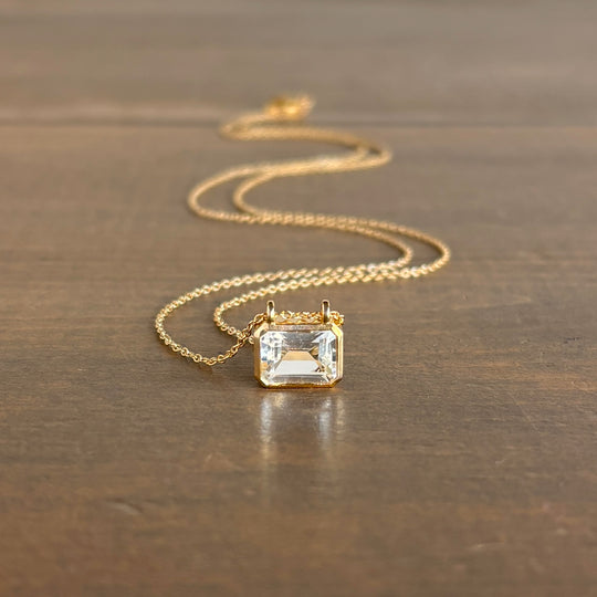 Gold necklace with a clear gemstone pendant on a wooden surface