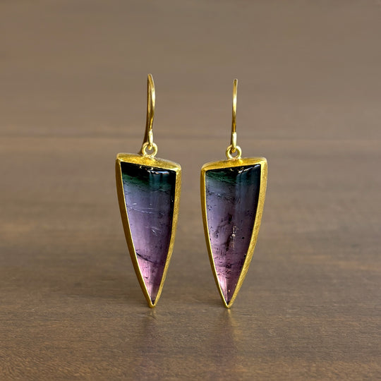 Gold-trimmed triangular earrings with purple and green gemstones on a brown background