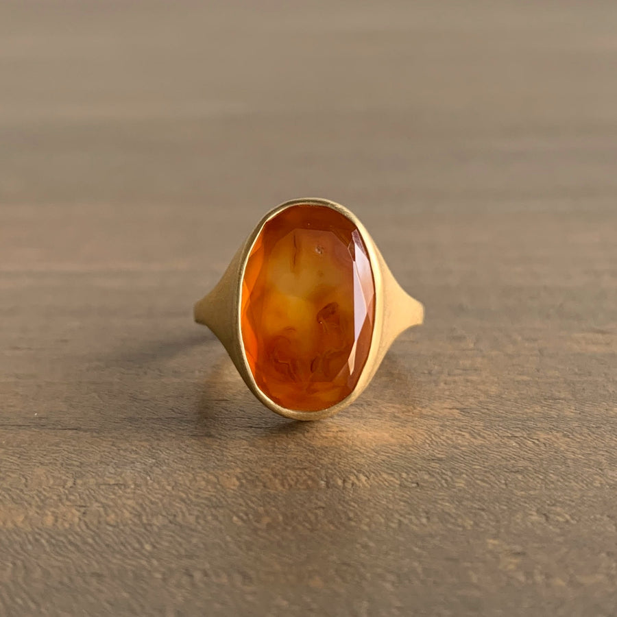 Gold ring with a large amber-colored stone on a wooden surface