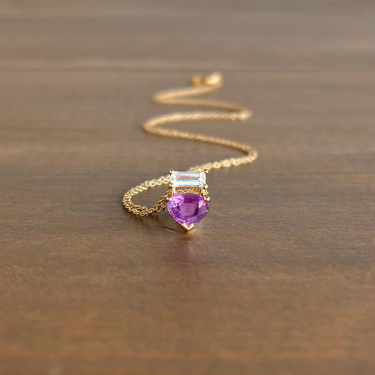 Gold necklace with a purple gemstone pendant on a wooden surface