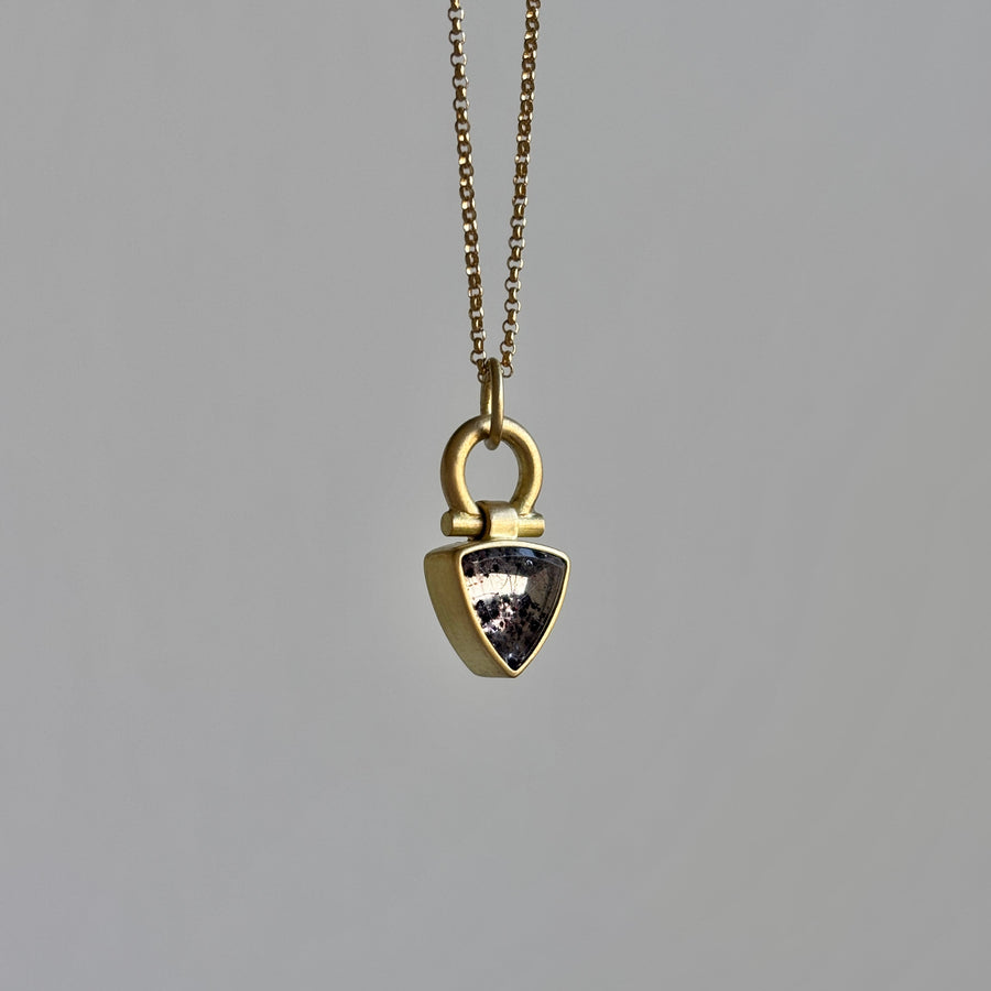 Gold necklace with a shield-shaped pendant on a gray background
