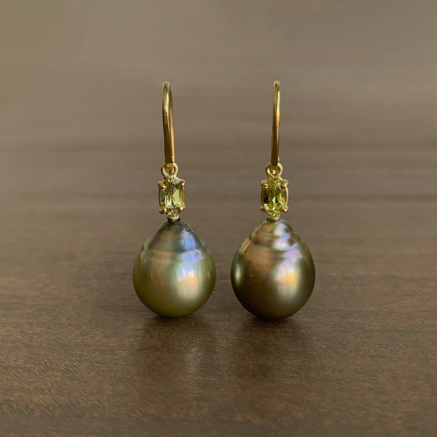 Pair of pearl earrings with gold hooks and green gemstones on a brown background