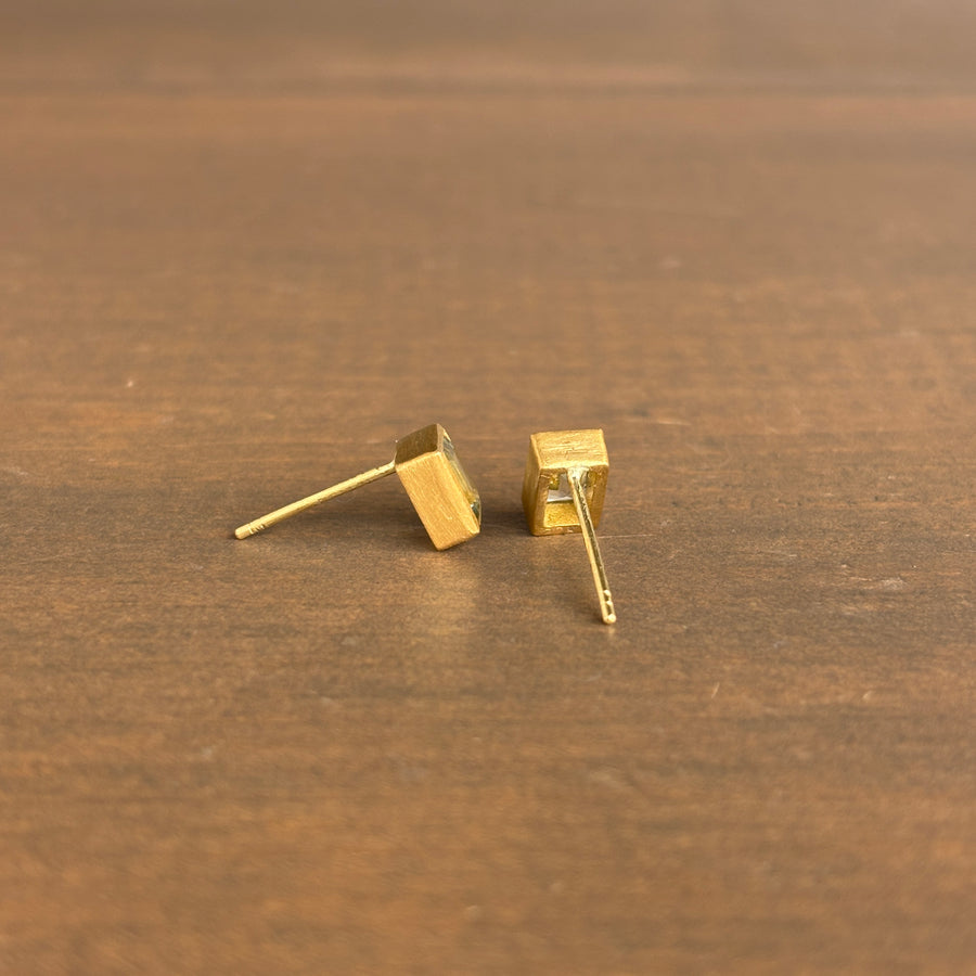 A pair of gold stud earrings back view of post, shown on a brown wooden surface. 