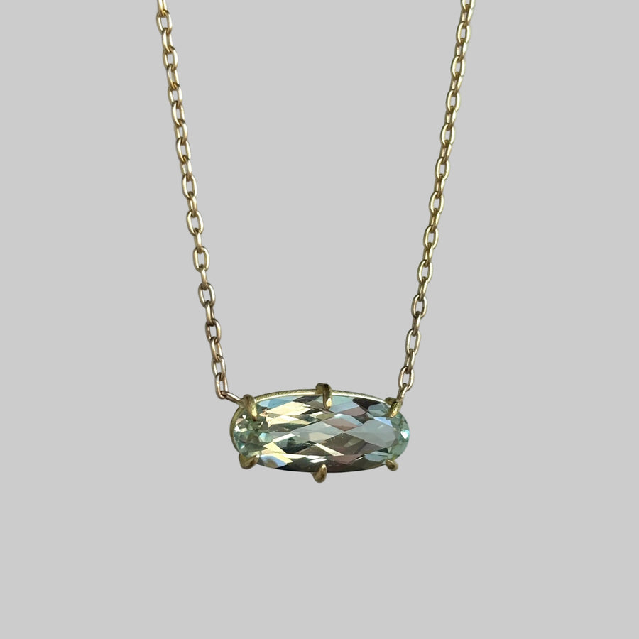 A gold chain necklace featuring an oval-cut light green gemstone pendant in a gold bezel setting, shown against a plain light gray background.