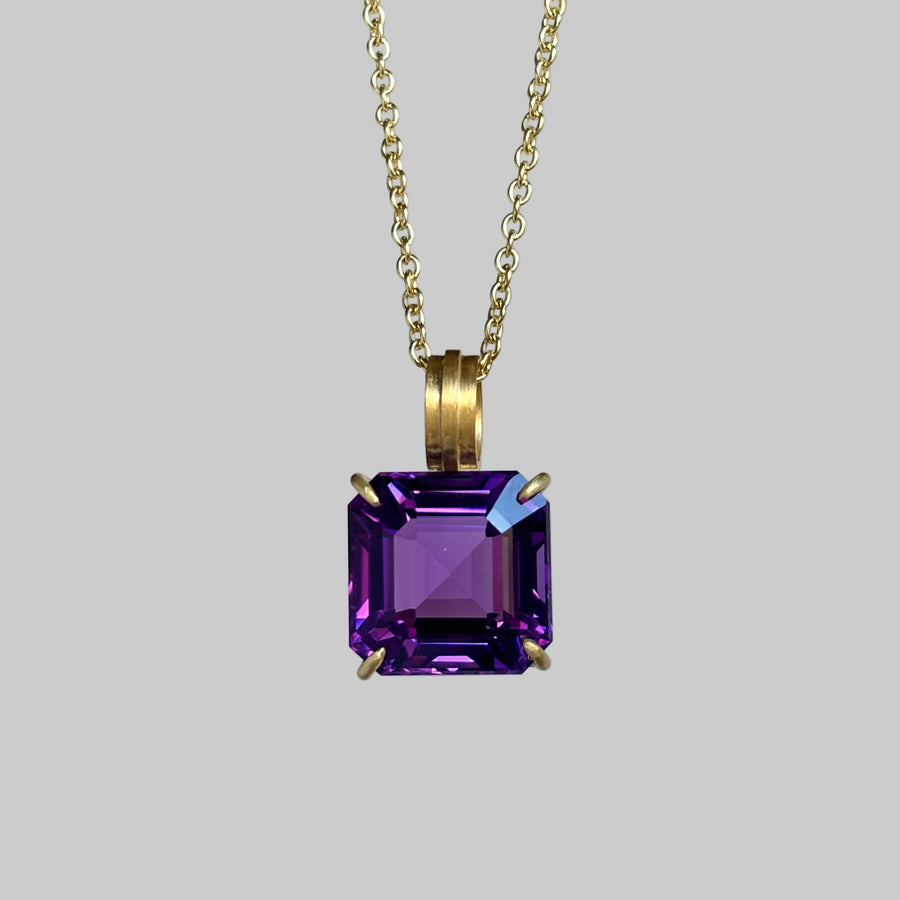 A gold chain necklace with a square-cut purple amethyst pendant in a four-prong setting, shown against a solid gray background.