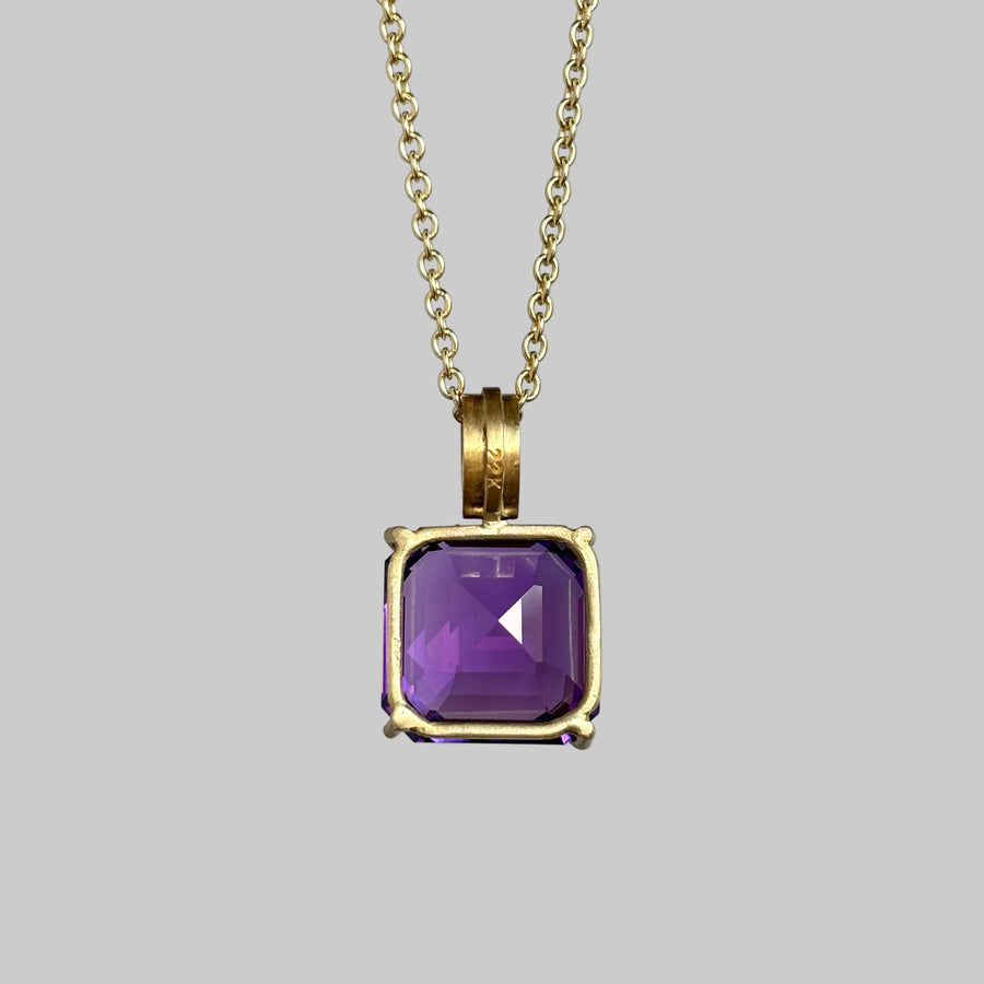 A gold chain necklace with a square bezel-set purple amethyst pendant, shown against a neutral gray background.