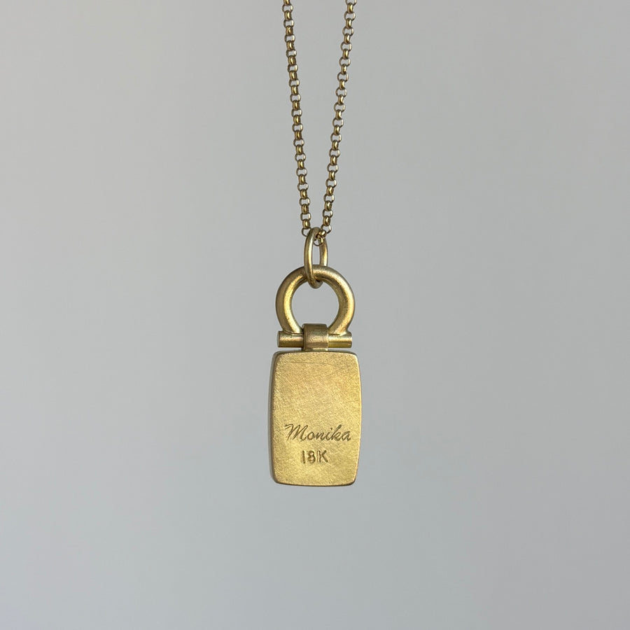 Gold necklace with a rectangular pendant on a gray background