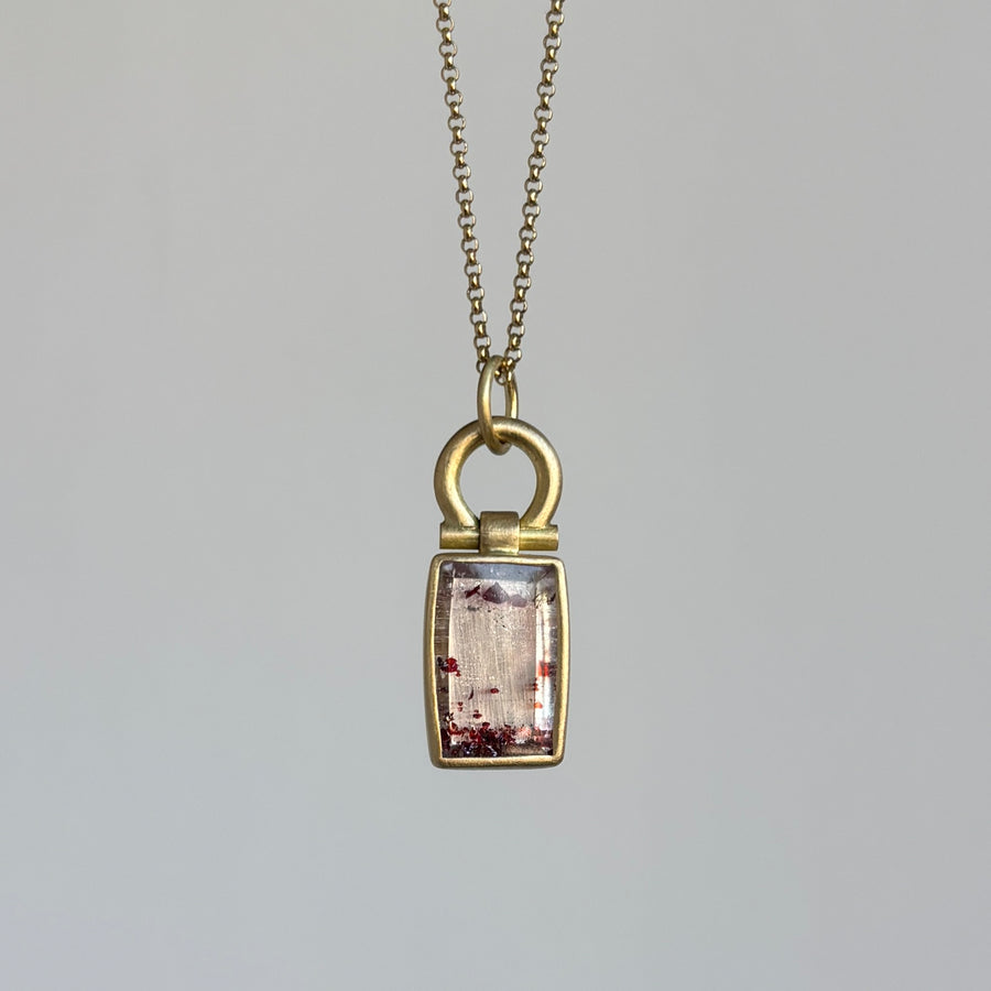 Gold pendant necklace with a rectangular gemstone on a gray background