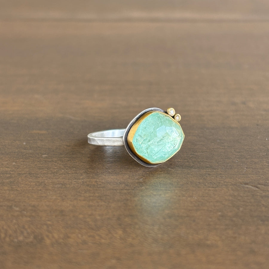 Ring with a blue gemstone, diamonds and gold accents on a wooden surface