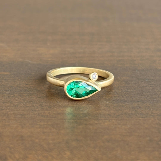 Gold ring with a green gemstone and a diamond on a wooden surface