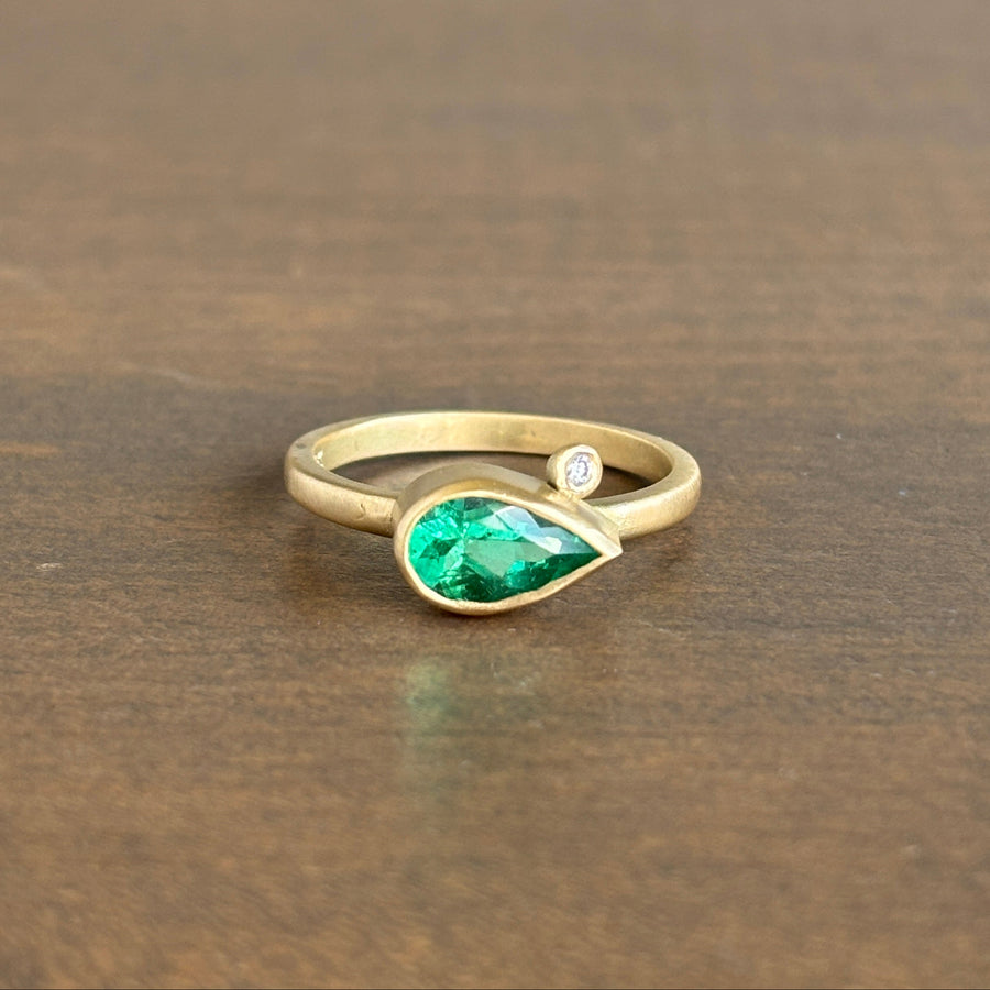 Gold ring with a green gemstone and a diamond on a wooden surface