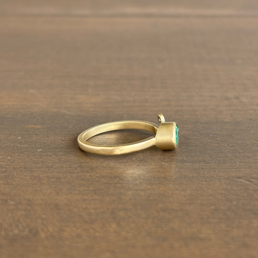 Gold ring with a green gemstone on a wooden surface