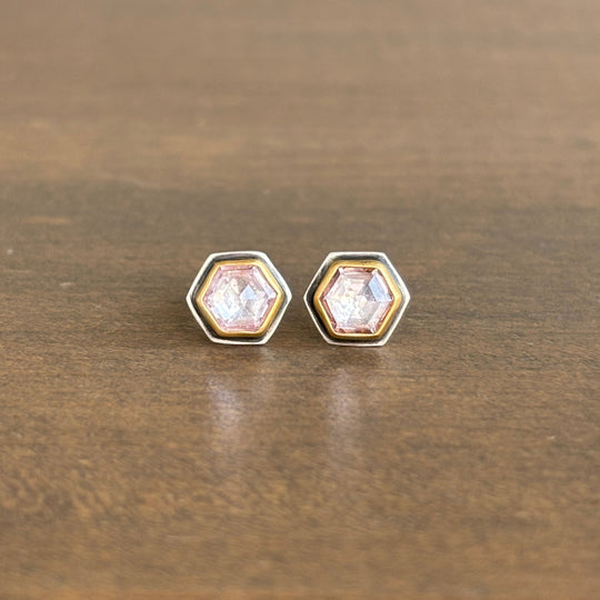 Hexagonal earrings with clear pink gemstones on a wooden surface