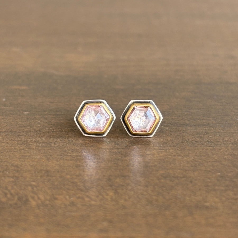 Hexagonal earrings with clear pink gemstones on a wooden surface