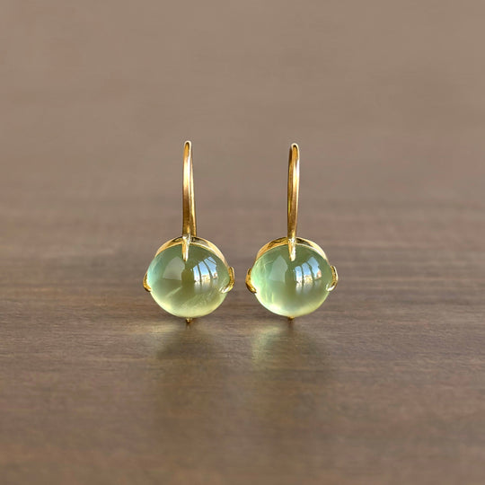Gold earrings with green gemstones on a wooden surface