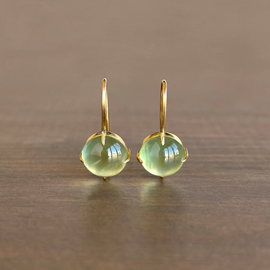 Gold earrings with green gemstones on a wooden surface