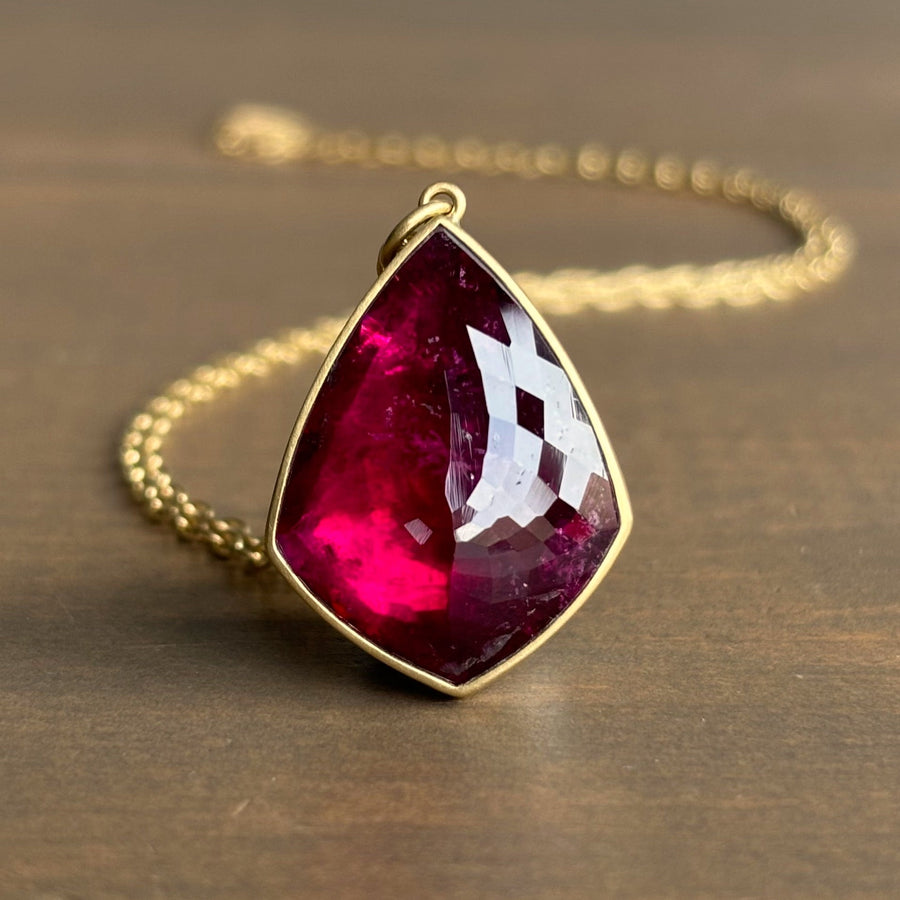 Gold necklace with a teardrop-shaped red gemstone pendant on a brown background