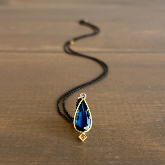 Necklace with a blue teardrop pendant on a wooden surface