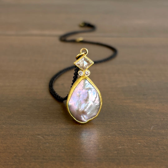 Gold pendant with a teardrop-shaped pearl and diamond-like stone on a wooden surface