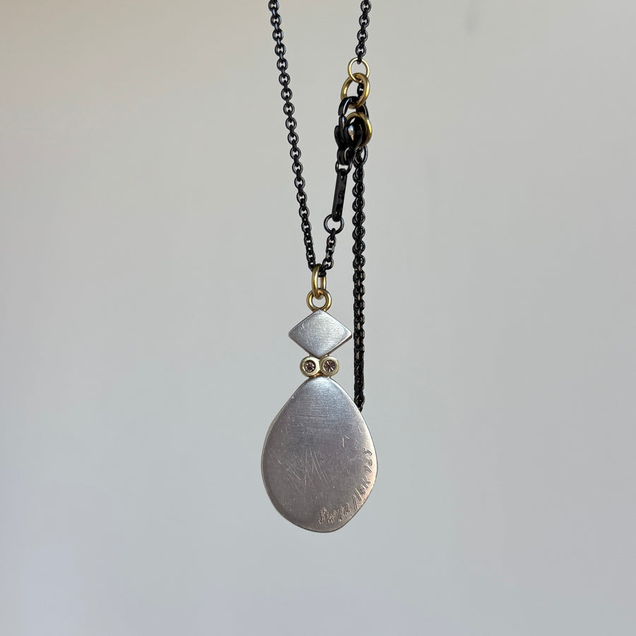 Necklace with a silver pendant on a black chain against a light gray background