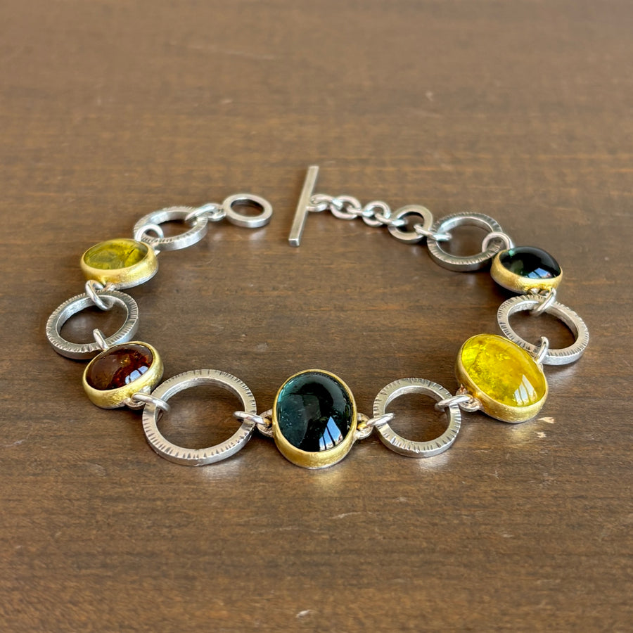 Silver bracelet with circular links and embedded gemstones on a wooden surface